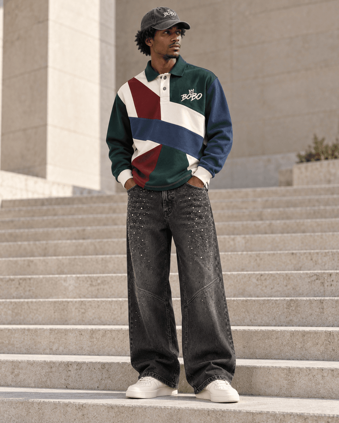 Full-body model in a BOBO patchwork rugby polo, crystal charcoal denim, grey crown cap and bone sneakers on concrete steps